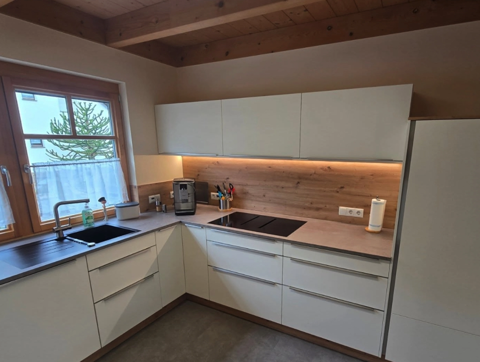 Küchenrenovierung mit Farbakzenten - Malerarbeiten und Wandgestaltung in einer Küche mit modernen weißen Schränken und Holzvertäfelung.