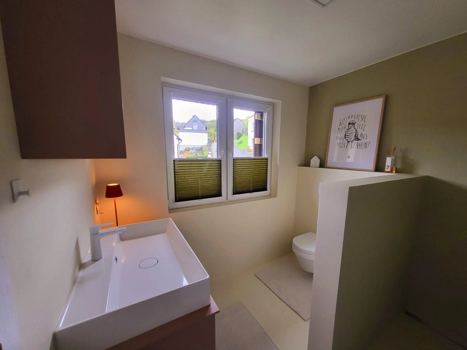 Badezimmer Renovierung - Malerarbeiten in einem Bad mit grünen und beigen Wänden, inklusive Fenster, Waschbecken und Toilette.